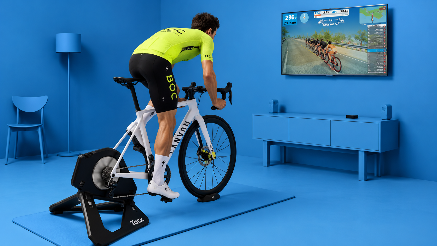 Rytter i BOC-drakt på sykkelrulle foran en TV med Zwift, i et blått rom